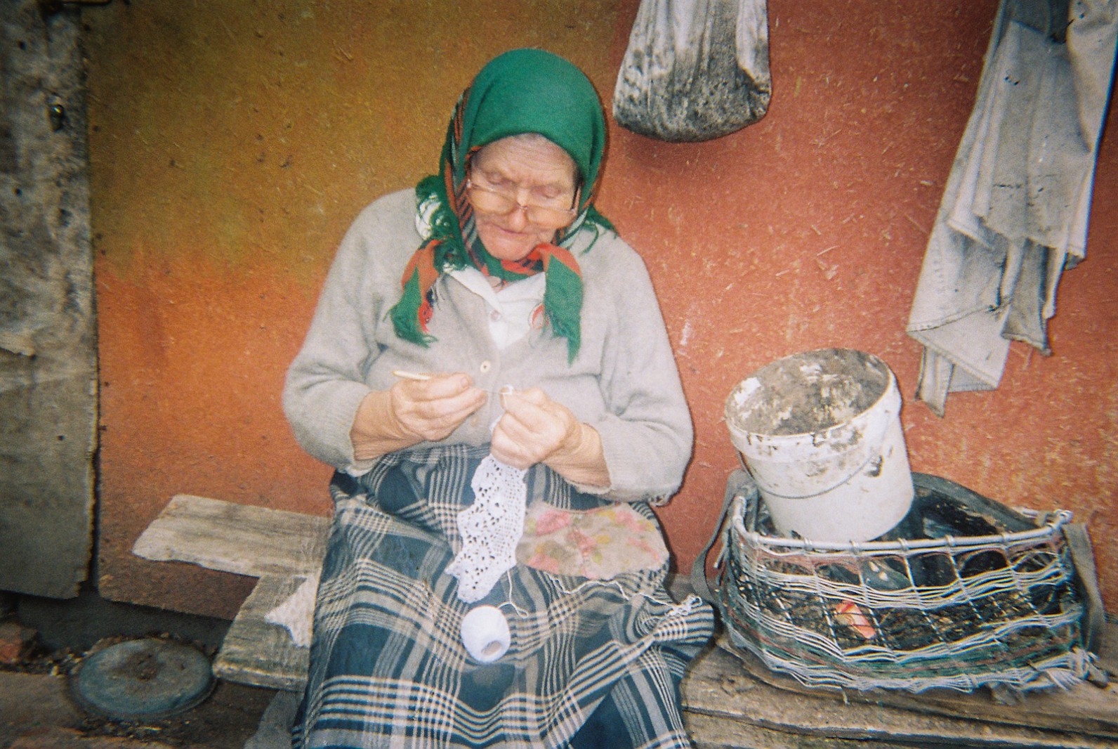 An elderly lady doing embroidery outside her  rural home