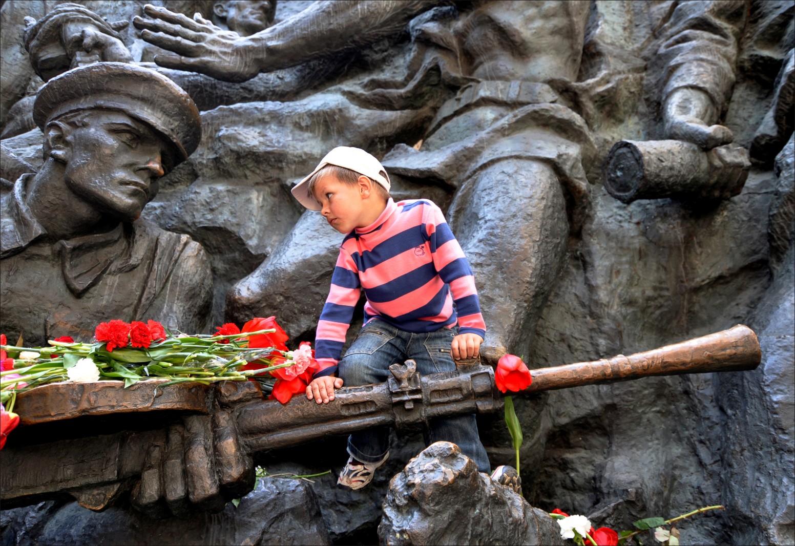 A young boy stares at a statue of USSR soldier as he climbs on a memorial to the Great Patriotic War in Kyiv